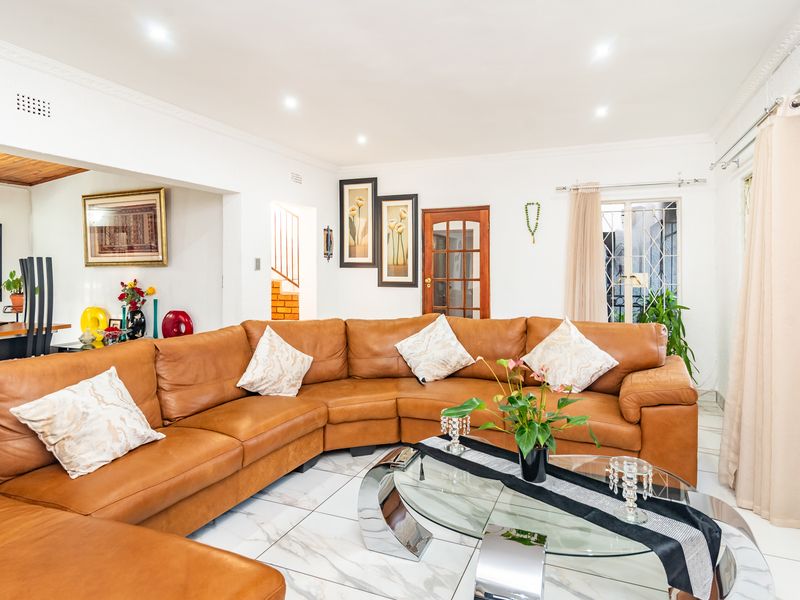 A bright living room featuring white tiled flooring, recessed downlighting, and crown molding, with an open-plan layout connecting to adjacent living spaces.