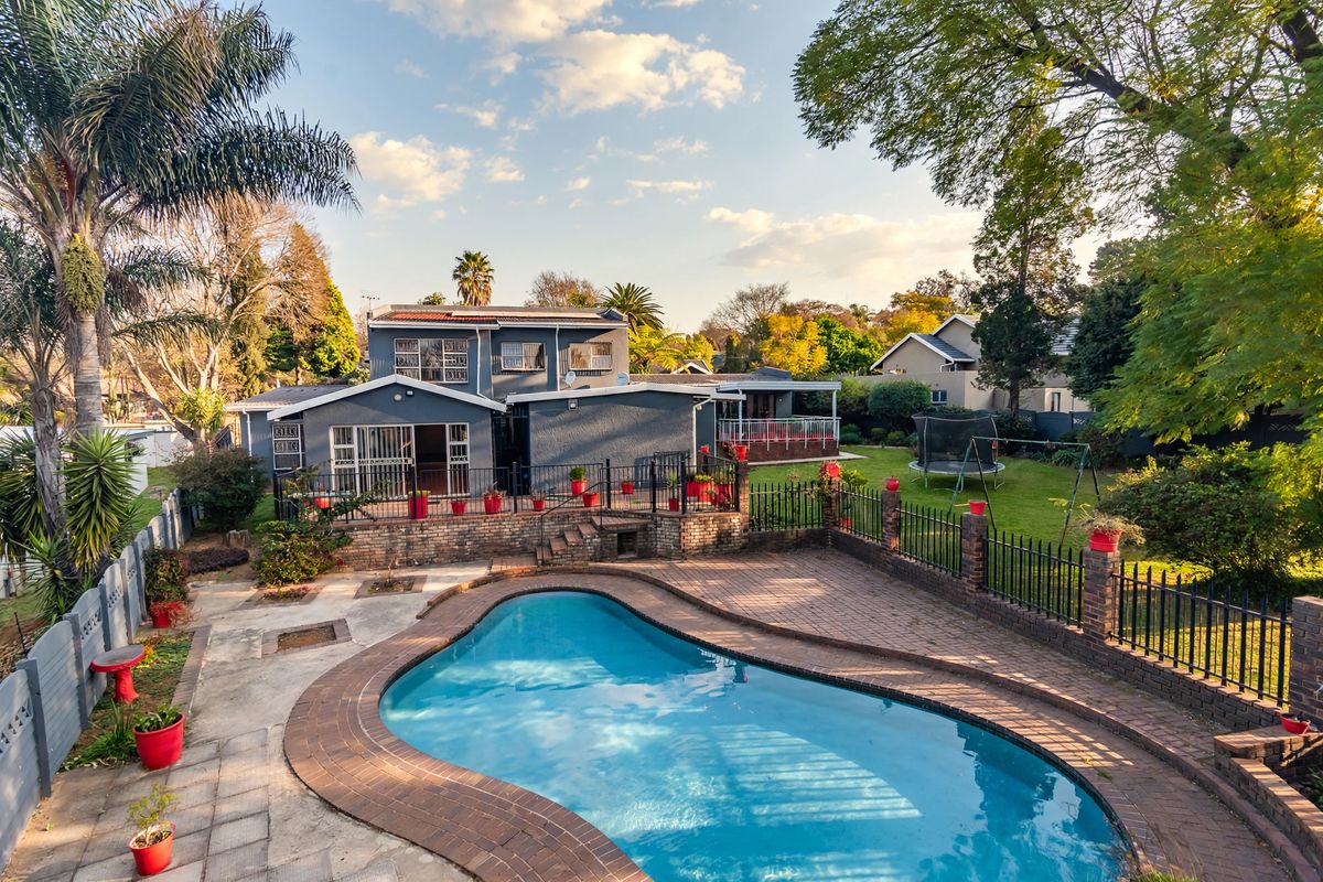 Rear view of the property featuring a swimming pool, paved patio area, and a spacious garden with established trees.