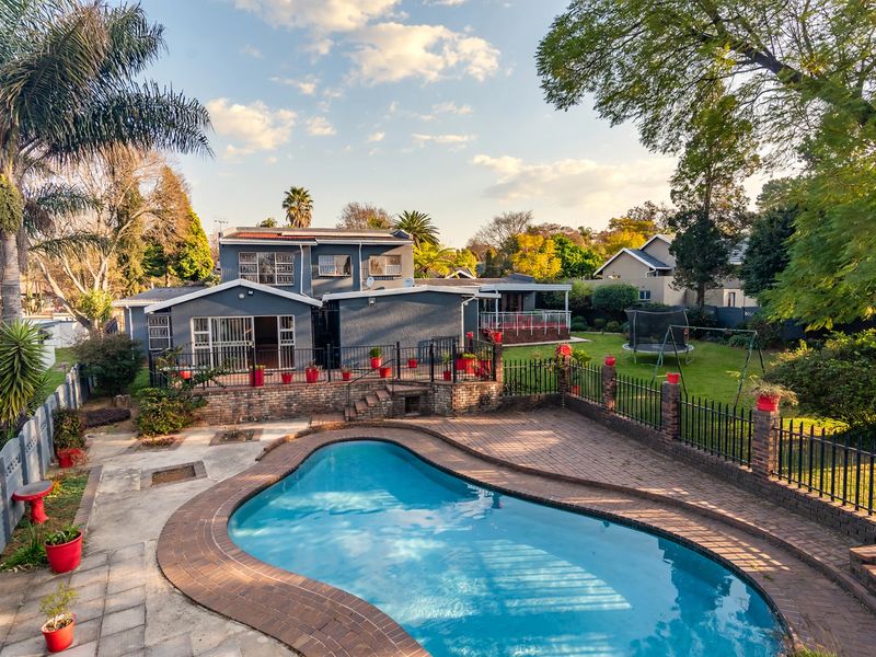 Rear view of the property featuring a swimming pool, paved patio area, and a spacious garden with established trees.