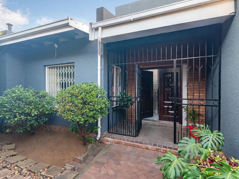 Front entrance of the house featuring a brick paved walkway, security gate, and timber front door with security bars on the windows.
