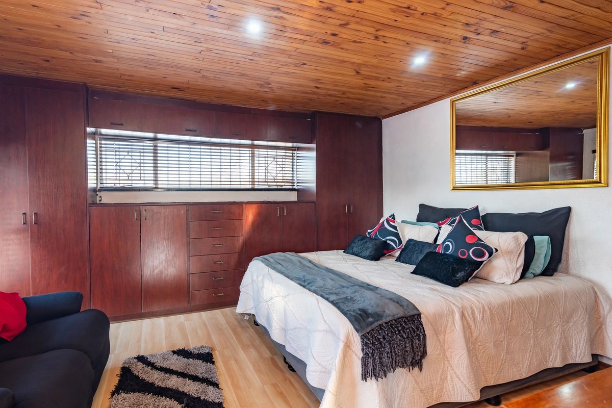 A bedroom featuring extensive built-in wooden cabinetry, a warm timber-clad ceiling with recessed lighting, and light-toned laminate flooring.