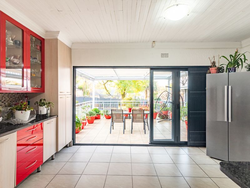 Open plan kitchen featuring red and wood-tone cabinetry, granite countertops, and large sliding doors opening onto a tiled patio area.