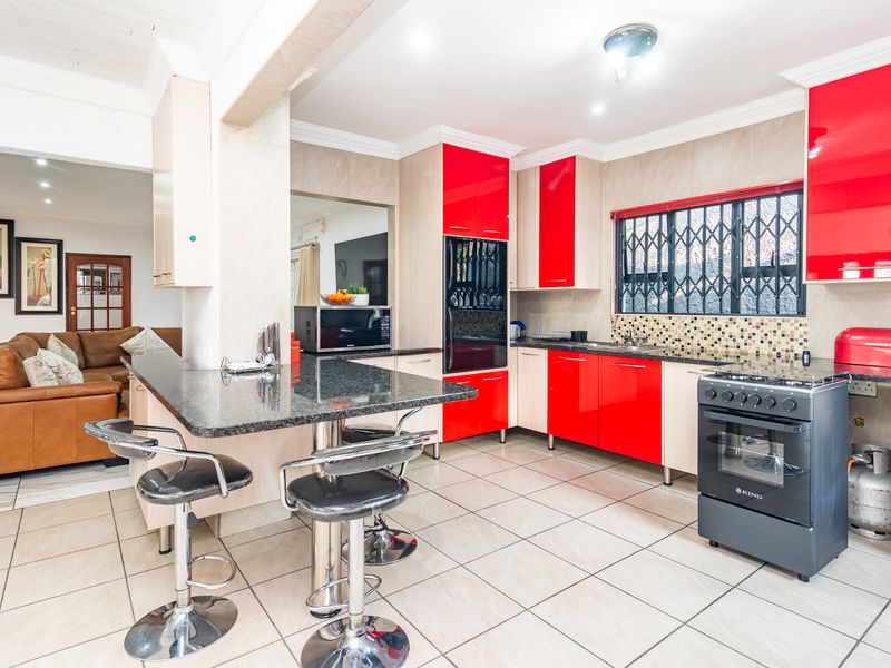 Open-plan kitchen featuring red cabinetry, granite countertops, a breakfast bar, and tiled flooring, seamlessly connecting to the adjacent living area.