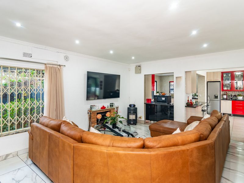 Spacious open-plan living area featuring marble-look tiled flooring, recessed lighting, a brick fireplace, and seamless flow into the adjacent kitchen.