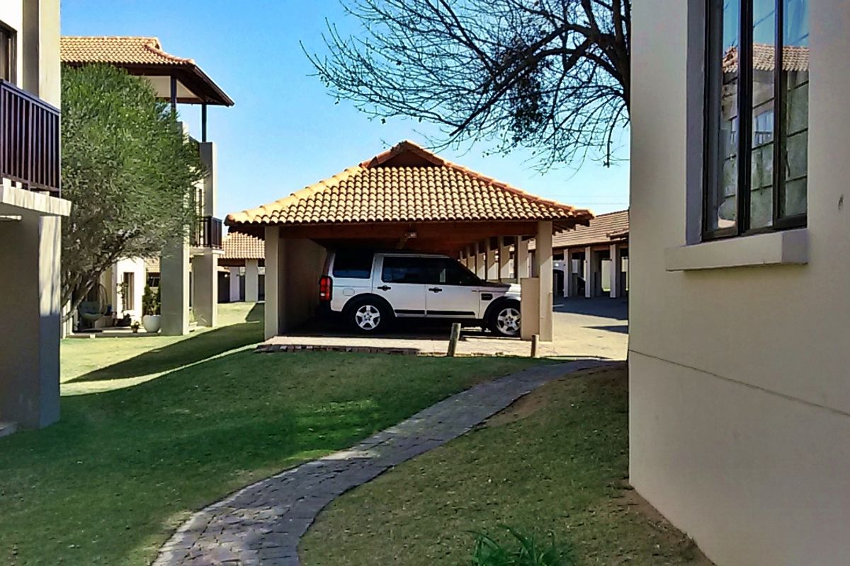 View of the apartment complex exterior featuring a covered carport, paved walkway, and well-maintained communal lawn area.