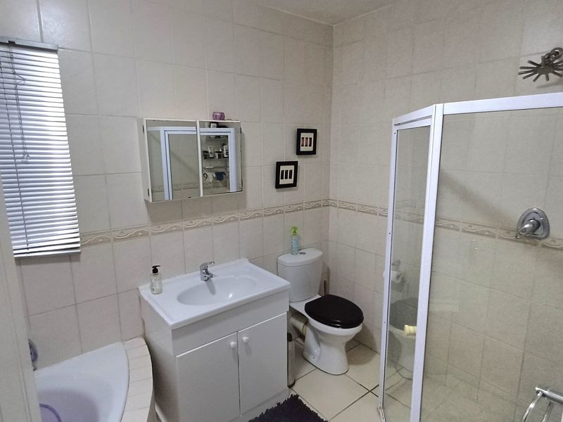 A functional bathroom featuring a corner bathtub, separate shower enclosure, vanity cabinet with basin, and tiled finishes throughout.