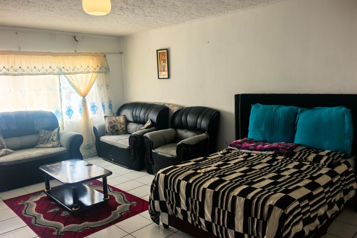 A bedroom featuring tiled flooring and a textured ceiling, currently furnished with a bed and seating area. The space requires cosmetic updates.