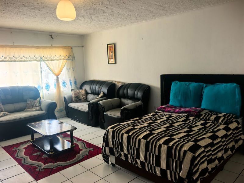 A bedroom featuring tiled flooring and a textured ceiling, currently furnished with a bed and seating area. The space requires cosmetic updates.