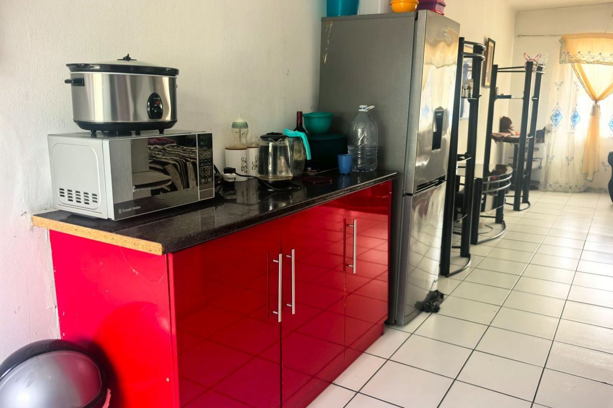 A compact kitchen area featuring vibrant red high-gloss cabinetry, dark granite countertops, and light-colored ceramic floor tiles.