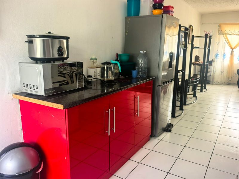 A compact kitchen area featuring vibrant red high-gloss cabinetry, dark granite countertops, and light-colored ceramic floor tiles.