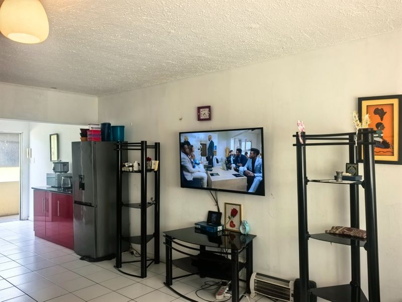 Open plan living area featuring tiled flooring and an adjacent kitchen with red cabinetry, showing signs of wear on the wall surfaces.