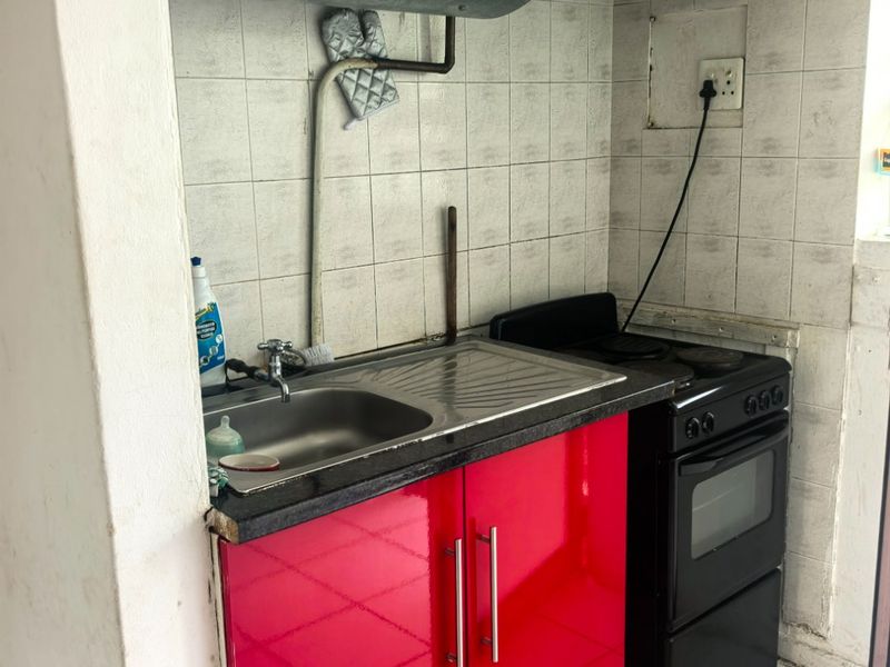 Compact kitchen area featuring a stainless steel sink, tiled backsplash, and a freestanding stove with an overhead extractor fan.