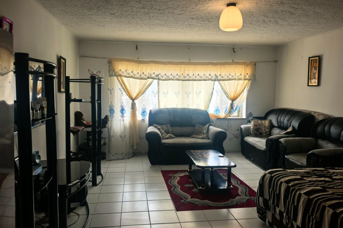 A living room featuring tiled flooring and a textured ceiling, currently requiring cosmetic updates to the wall finishes and general maintenance.