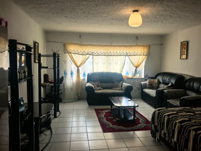 A living room featuring tiled flooring and a textured ceiling, currently requiring cosmetic updates to the wall finishes and general maintenance.