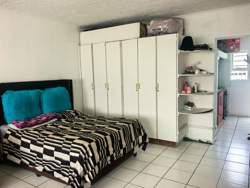 Bedroom featuring built-in white wardrobes, ceramic floor tiles, and a textured ceiling, with an adjacent view into the kitchen area.