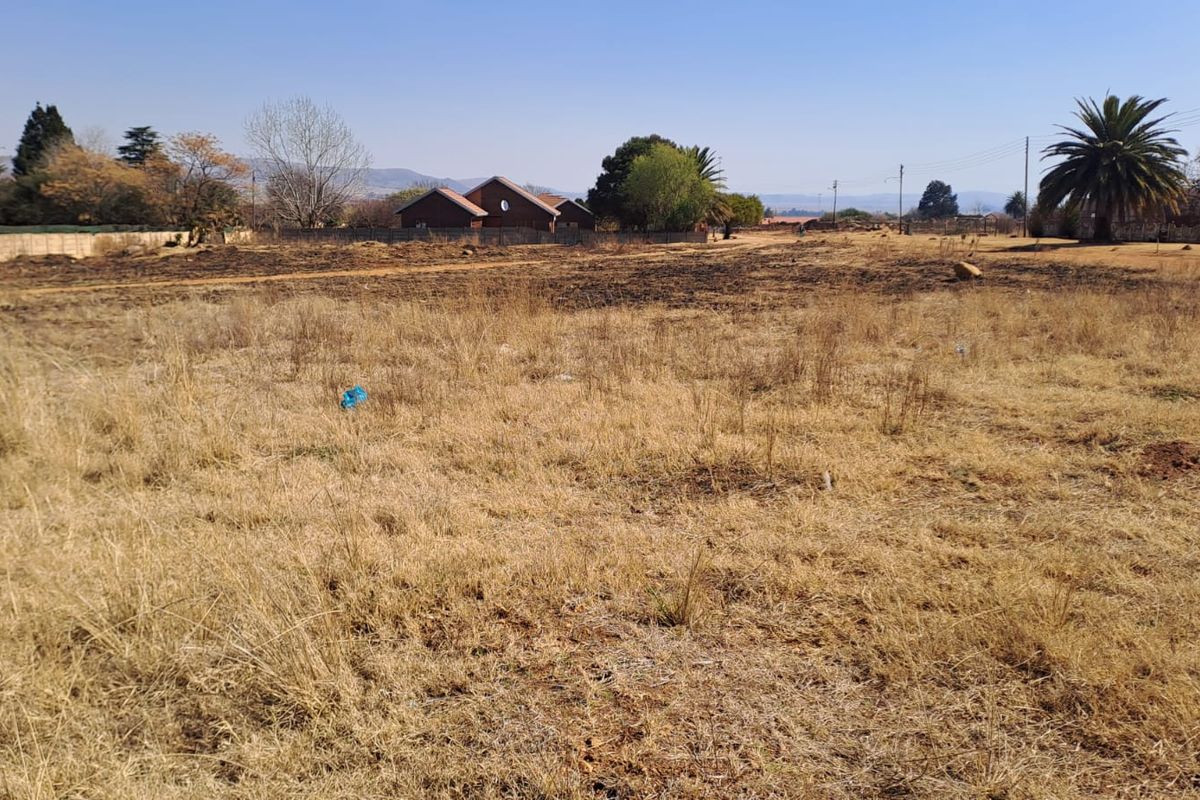 A wide-angle view of a vacant residential plot featuring dry grass and perimeter fencing, suitable for future development.