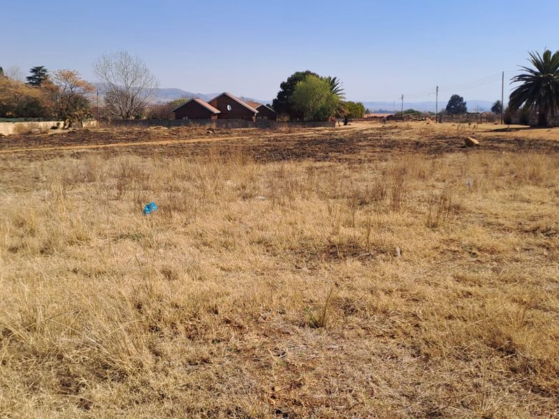 A wide-angle view of a vacant residential plot featuring dry grass and perimeter fencing, suitable for future development.