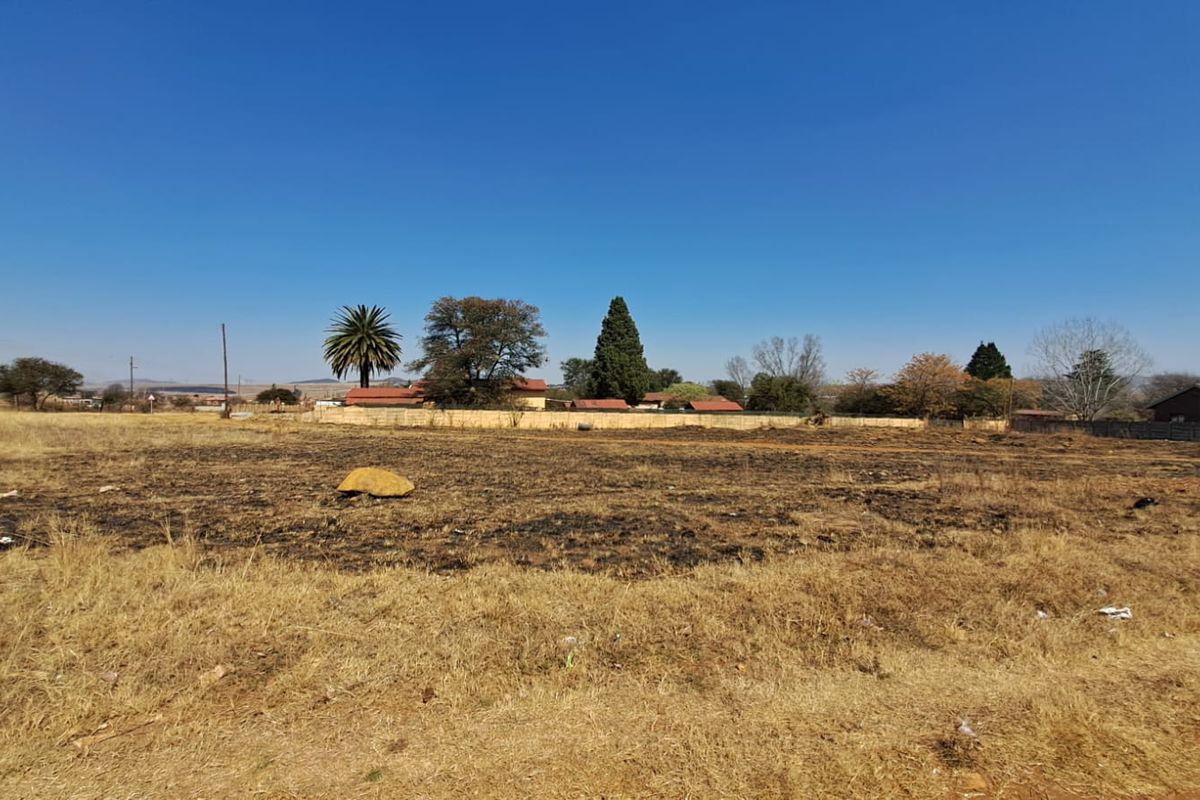 A view of a vacant residential plot of land with dry grass and a boundary wall in the background.