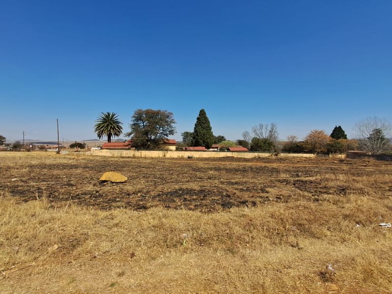 A view of a vacant residential plot of land with dry grass and a boundary wall in the background.