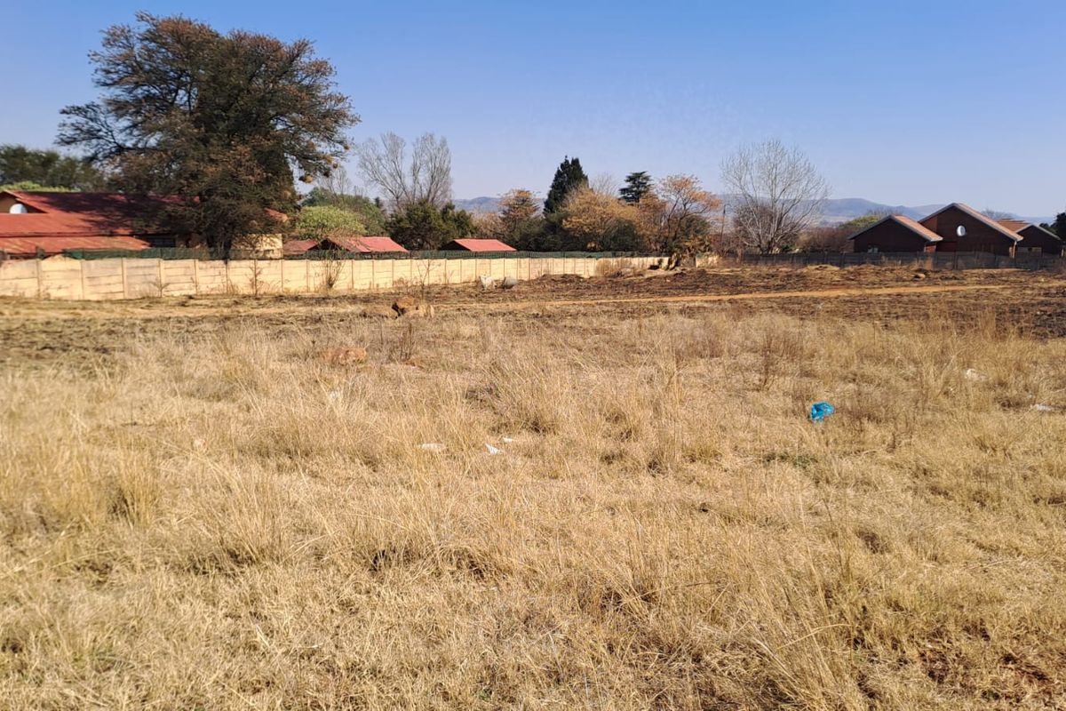 A view of a vacant residential plot featuring dry grass and a perimeter wall, suitable for future development.