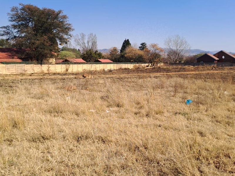 A view of a vacant residential plot featuring dry grass and a perimeter wall, suitable for future development.