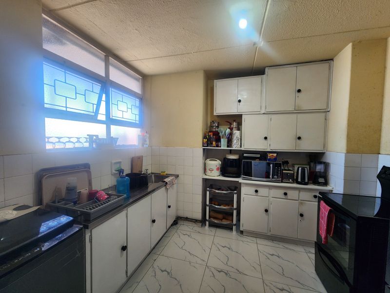 A functional kitchen featuring built-in white cabinetry, a stainless steel sink, tiled backsplash, and tiled flooring, offering potential for modernization.