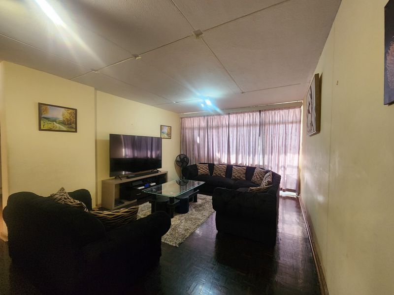 A living room featuring dark parquet flooring and traditional ceiling tiles, offering a functional space with potential for modernization.
