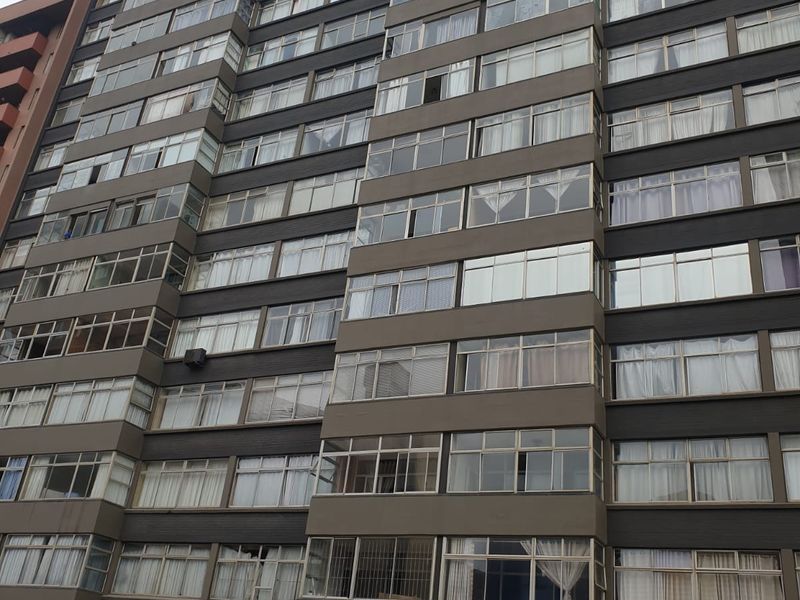 A multi-story apartment building facade featuring numerous windows and a ground-level entrance canopy.