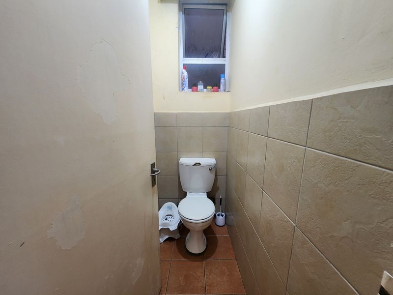 A small bathroom featuring a standard toilet, tiled flooring, and tiled wall accents, currently showing signs of wear on the painted wall surfaces.