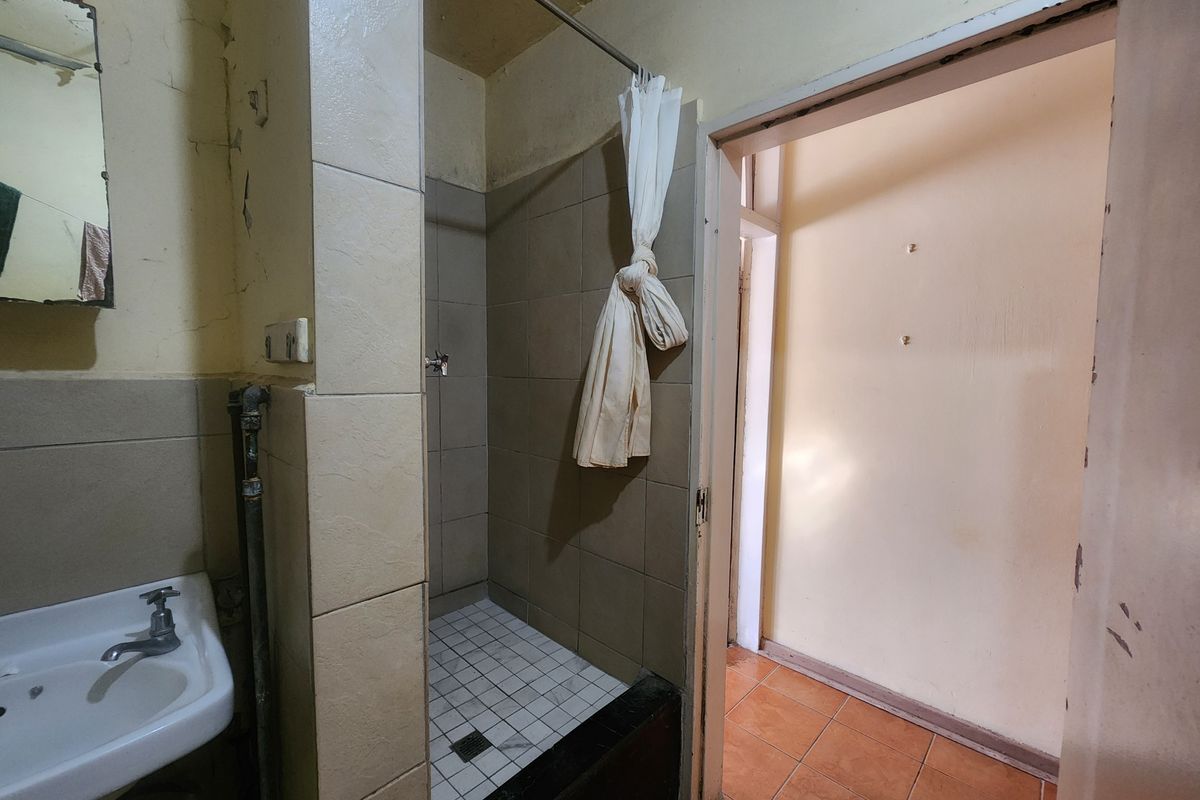 A dated bathroom featuring a tiled shower enclosure and pedestal basin, requiring significant cosmetic updates and repairs to wall finishes.