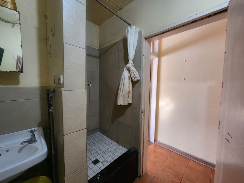 A dated bathroom featuring a tiled shower enclosure and pedestal basin, requiring significant cosmetic updates and repairs to wall finishes.