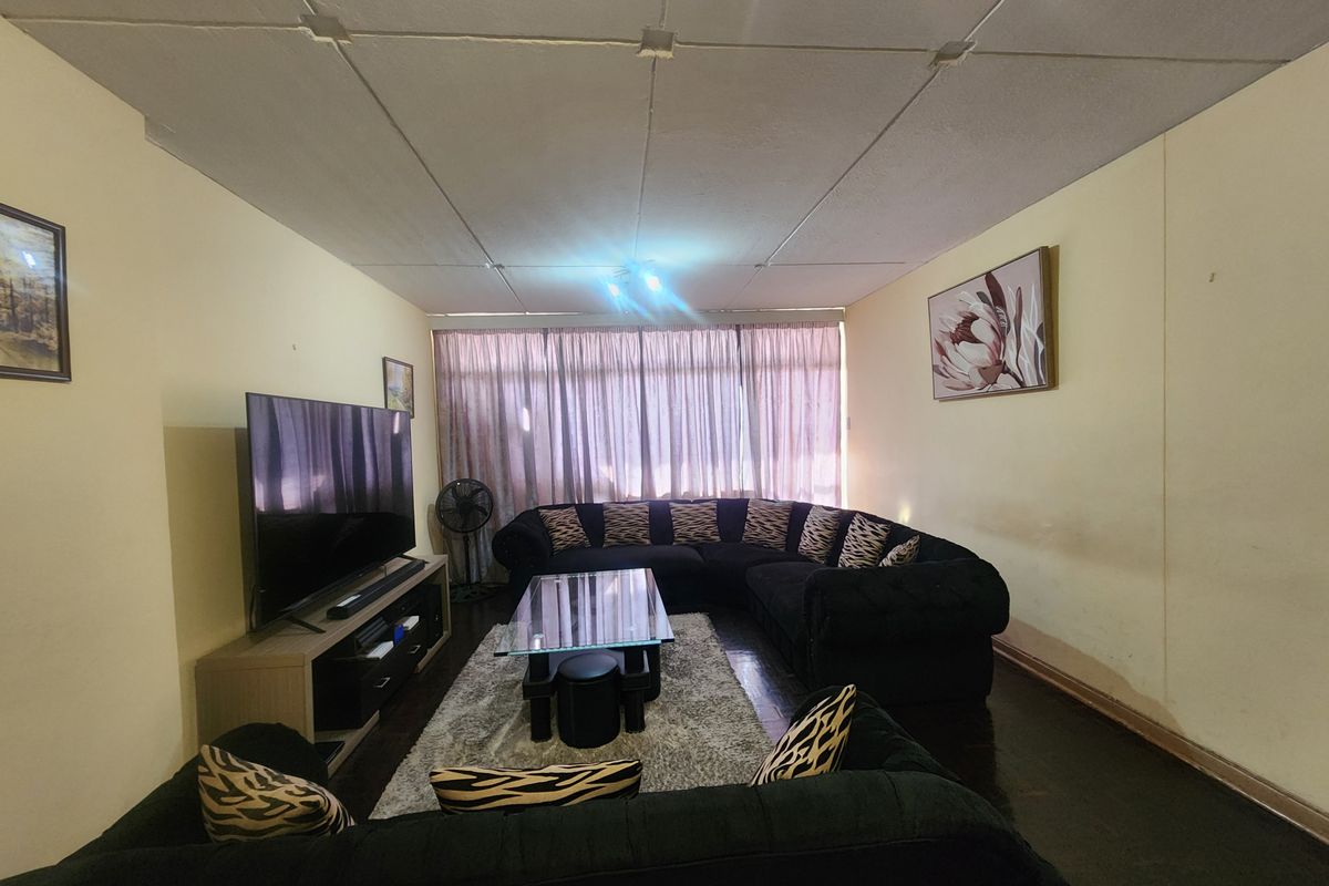 A living room featuring parquet flooring and a tiled ceiling, offering a functional space that would benefit from cosmetic updates and modern finishes.