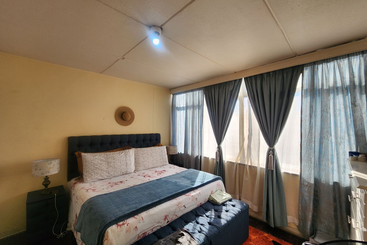 A bedroom featuring a large window with curtains and a tiled ceiling, offering a functional space with potential for cosmetic updates.