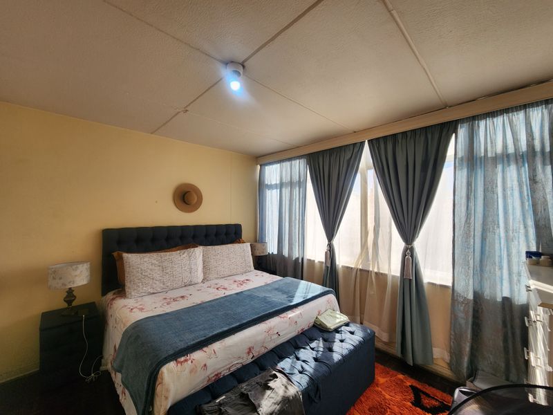 A bedroom featuring a large window with curtains and a tiled ceiling, offering a functional space with potential for cosmetic updates.