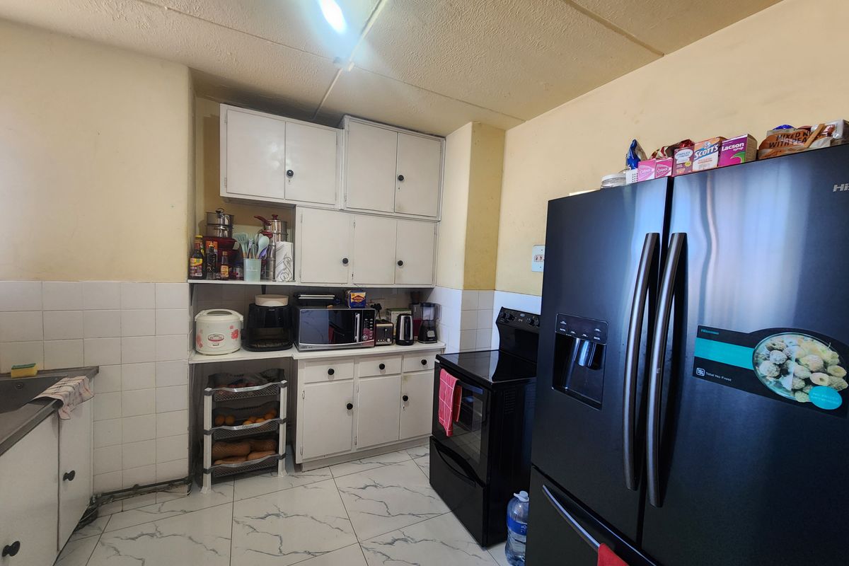 A functional kitchen featuring white cabinetry, tiled backsplash, and marble-look flooring, offering a practical layout with potential for modern cosmetic updates.