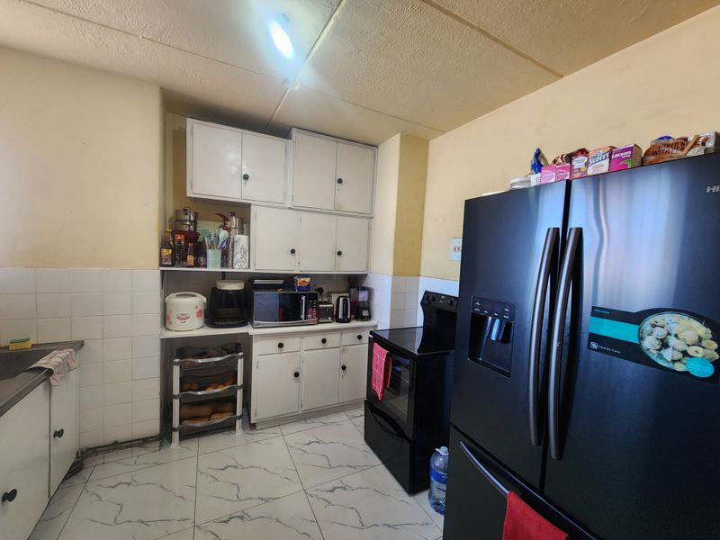 A functional kitchen featuring white cabinetry, tiled backsplash, and marble-look flooring, offering a practical layout with potential for modern cosmetic updates.