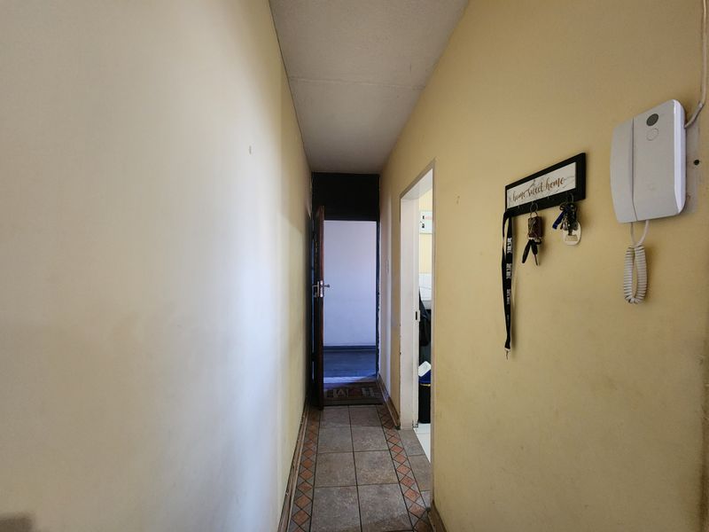 A narrow apartment hallway featuring tiled flooring and an installed intercom system, leading towards an entrance door.