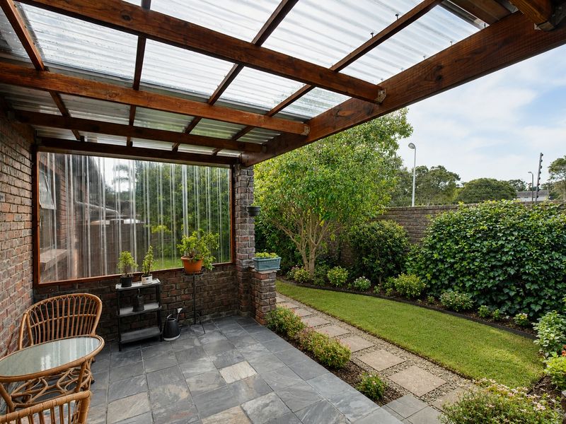 A covered patio featuring a timber pergola with a corrugated roof, slate tile flooring, and direct access to a landscaped garden with a paved path.