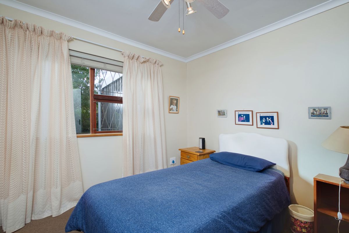 A standard bedroom featuring a ceiling fan, neutral wall finishes, and a window with timber framing.