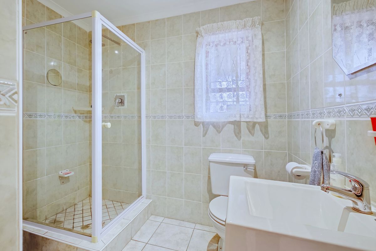 A functional bathroom featuring a glass-enclosed shower, tiled walls and flooring, a standard toilet, and a vanity basin with a chrome mixer tap.