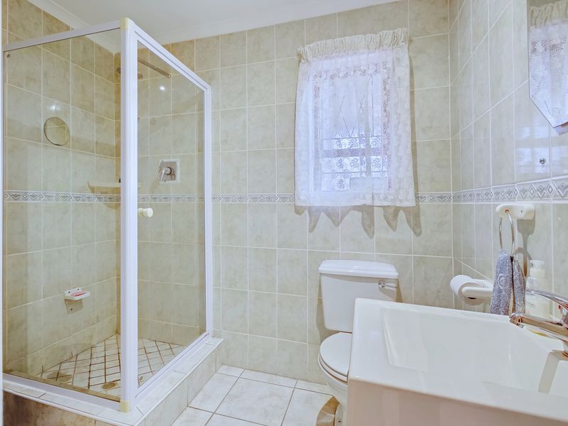 A functional bathroom featuring a glass-enclosed shower, tiled walls and flooring, a standard toilet, and a vanity basin with a chrome mixer tap.