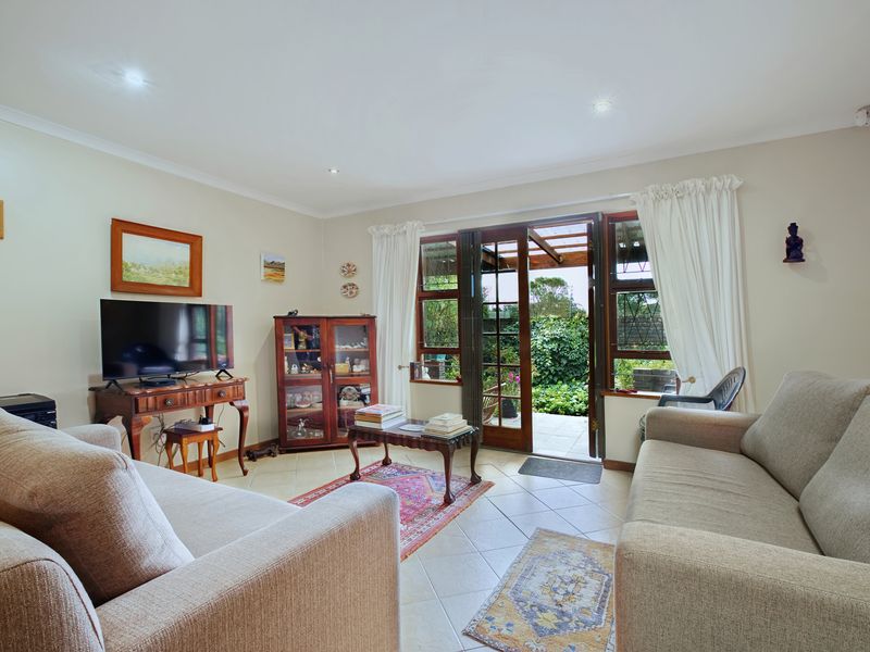 A comfortable living room featuring tiled flooring, recessed lighting, and timber-framed glass doors providing direct access to the rear patio and garden.