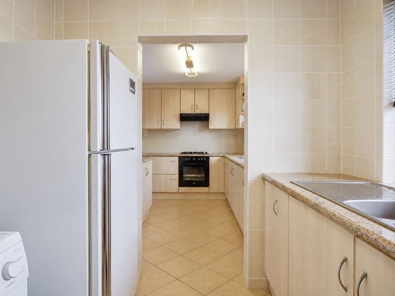A functional kitchen featuring light wood cabinetry, tiled splashbacks, a built-in oven with gas hob, and a double-basin stainless steel sink.