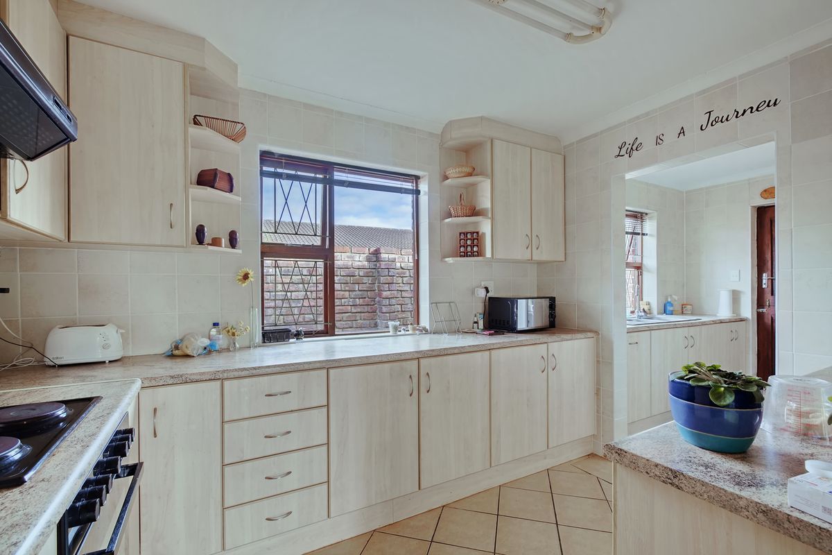 A functional kitchen featuring light wood-finish cabinetry, tiled backsplash, and durable ceramic flooring, with an adjacent scullery area visible through the opening.