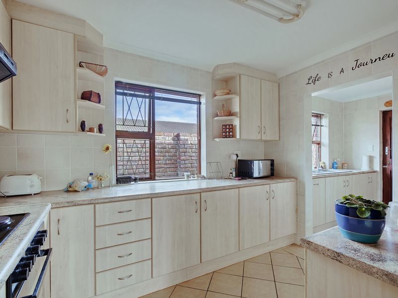 A functional kitchen featuring light wood-finish cabinetry, tiled backsplash, and durable ceramic flooring, with an adjacent scullery area visible through the opening.