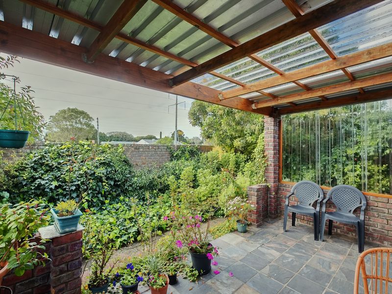A covered patio area featuring a timber pergola with corrugated roofing, slate tile flooring, and brick structural elements, overlooking a private garden.