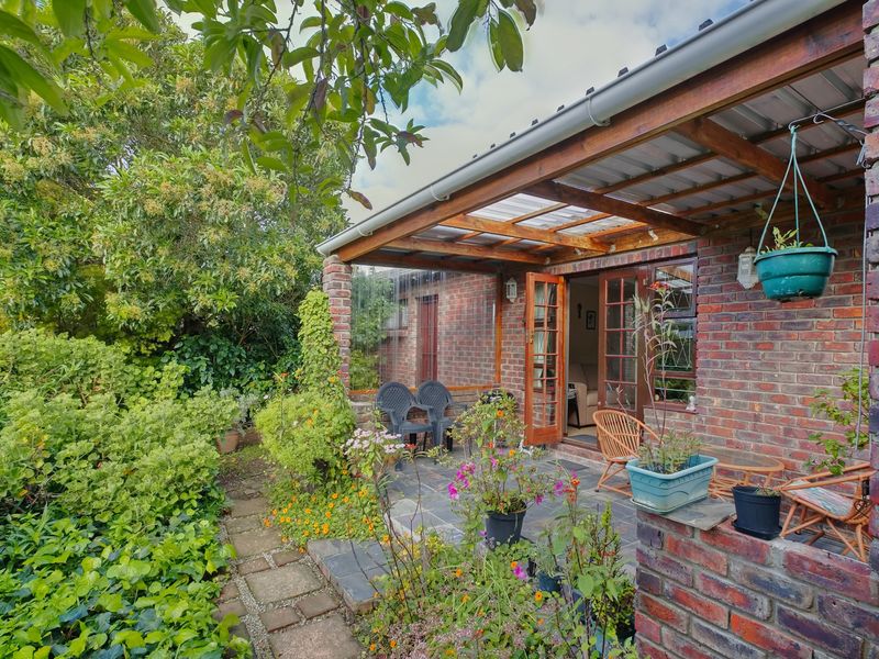 A covered outdoor patio featuring exposed brick walls, slate flooring, and timber-framed french doors leading into the home, surrounded by a lush garden.