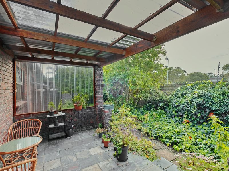 Covered patio area featuring a timber pergola with polycarbonate roofing, exposed brickwork, and slate tile flooring, overlooking a private garden space.
