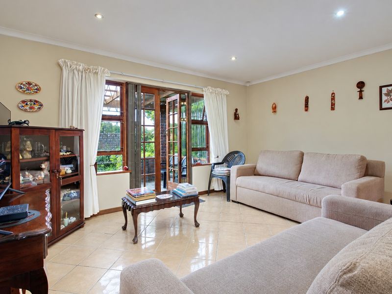 A comfortable living room featuring tiled flooring, recessed downlights, and wooden framed glass doors providing access to the outdoor area.