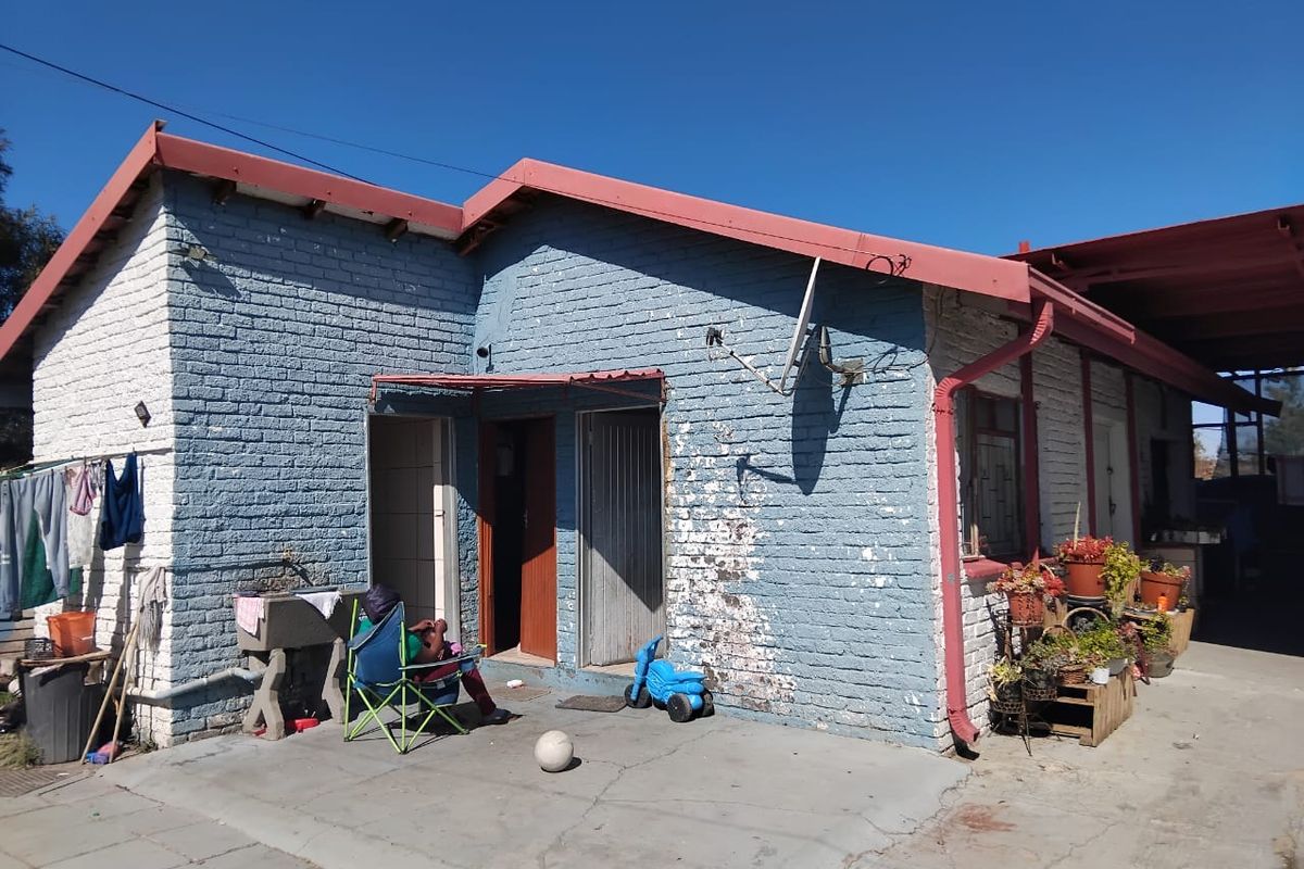 Rear view of a single-story brick house featuring a concrete patio area, metal roofing, and external wash basin.